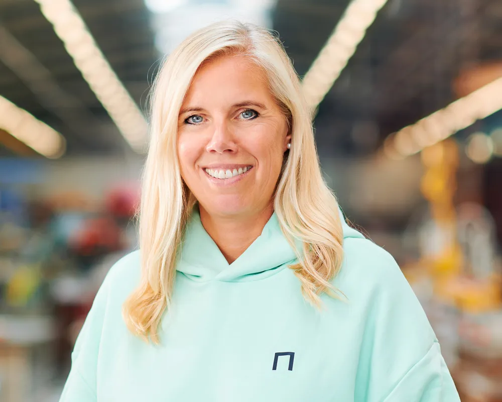 Eine blonde Frau, Leiterin der Abteilung Marketing & Kommunikation, trägt einen Pullover mit dem Firmenlogo der Jansen Group und lächelt in die Kamera.