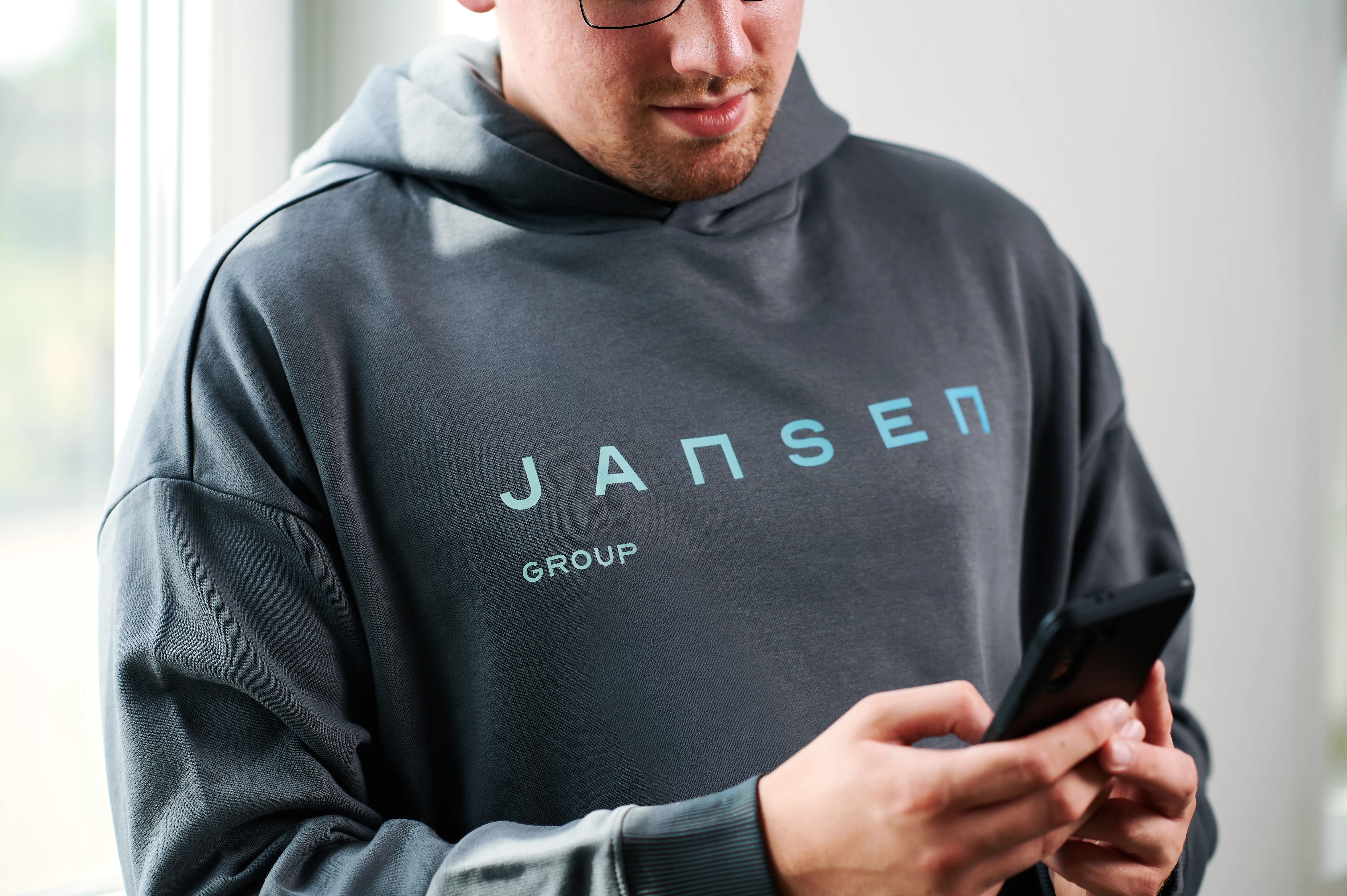 Ein Mann, der einen grauen Pullover mit dem Firmenlogo der Jansen Group trägt, schaut auf sein Handy.